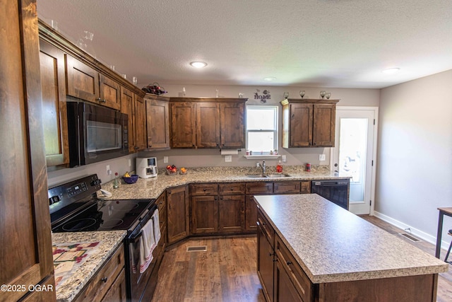 kitchen featuring dark wood-type flooring, visible vents, black appliances, and a sink