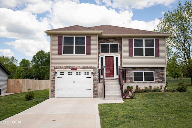 raised ranch with fence, an attached garage, stone siding, concrete driveway, and a front lawn