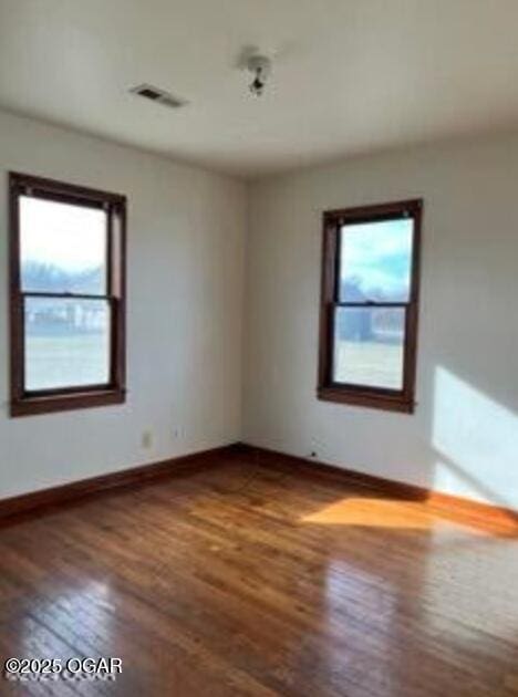 empty room with visible vents, baseboards, plenty of natural light, and wood finished floors