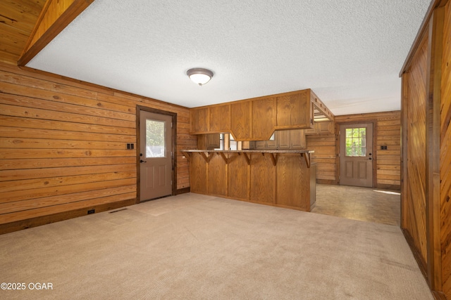 6309 Impala Dr, Joplin, MO 64804 - kitchen featuring a breakfast bar area, wood walls, brown cabinets, light carpet, and a textured ceiling