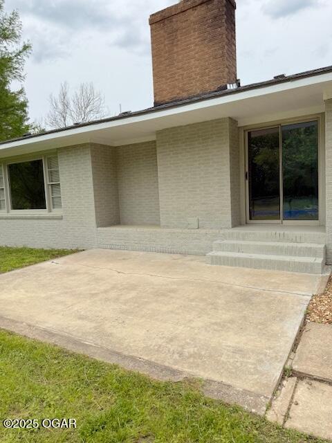 property entrance with a patio, a chimney, and brick siding