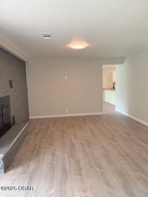unfurnished living room with light wood-type flooring, visible vents, baseboards, and a textured ceiling
