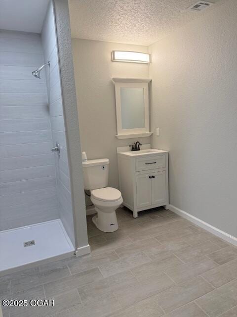 full bath featuring a textured ceiling, toilet, visible vents, tiled shower, and vanity