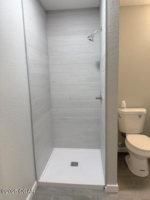 bathroom with a stall shower, baseboards, toilet, and a textured wall