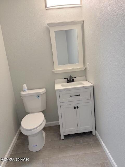 half bathroom with vanity, toilet, baseboards, and tile patterned flooring