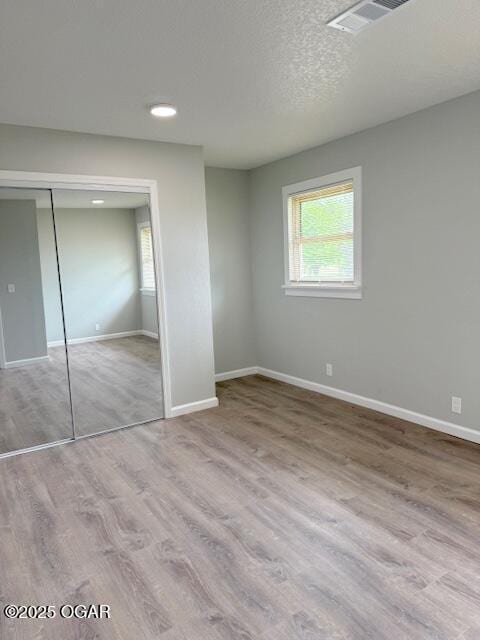 unfurnished bedroom with baseboards, a closet, visible vents, and wood finished floors