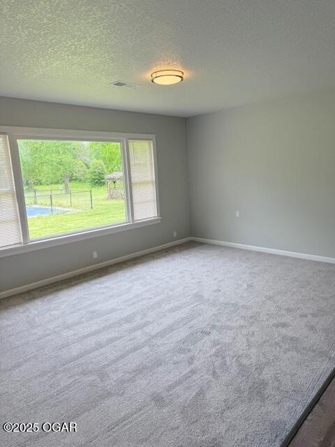 empty room featuring a textured ceiling, carpet, and baseboards