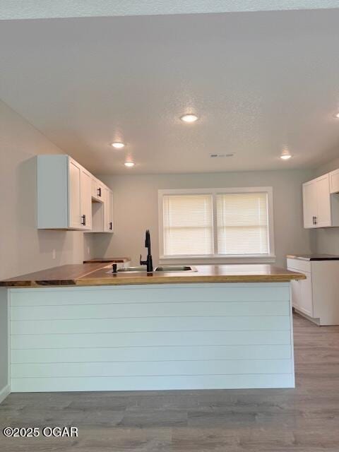 kitchen featuring a peninsula, light wood-style flooring, a sink, white cabinetry, and recessed lighting