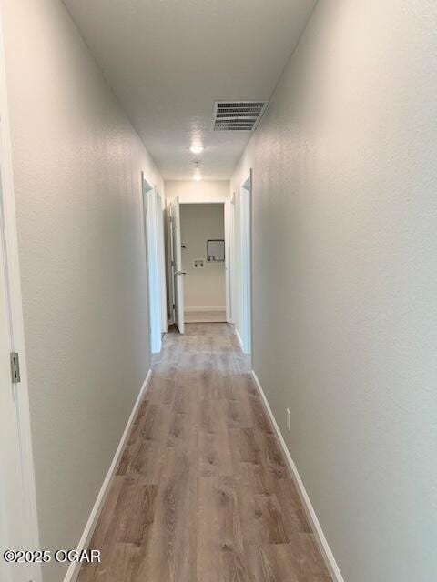 hallway with baseboards, visible vents, and light wood-style floors
