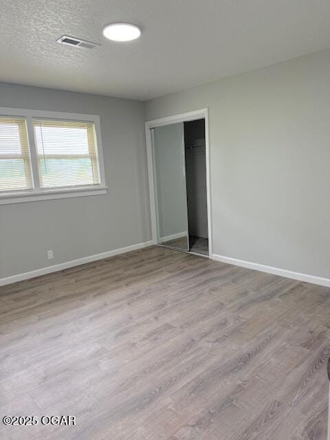unfurnished bedroom featuring baseboards, a closet, visible vents, and wood finished floors