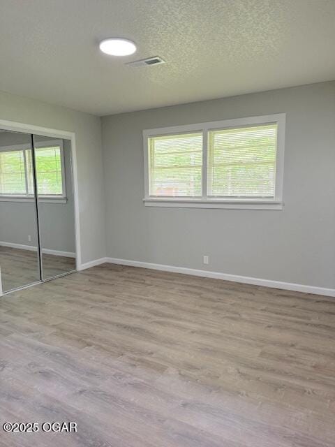 spare room with light wood-type flooring, visible vents, baseboards, and a textured ceiling