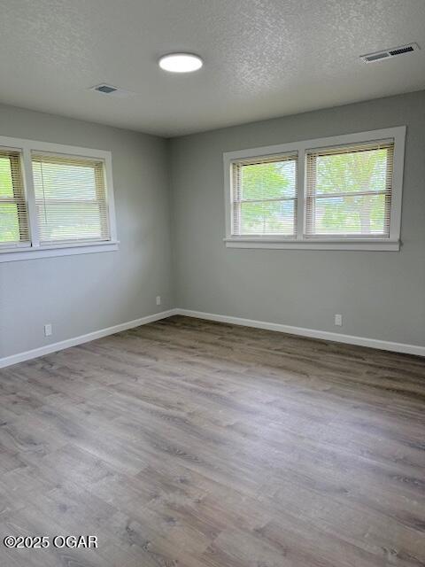 spare room with a textured ceiling, baseboards, visible vents, and wood finished floors