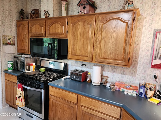 kitchen featuring black microwave, stainless steel gas stove, wallpapered walls, and brown cabinetry