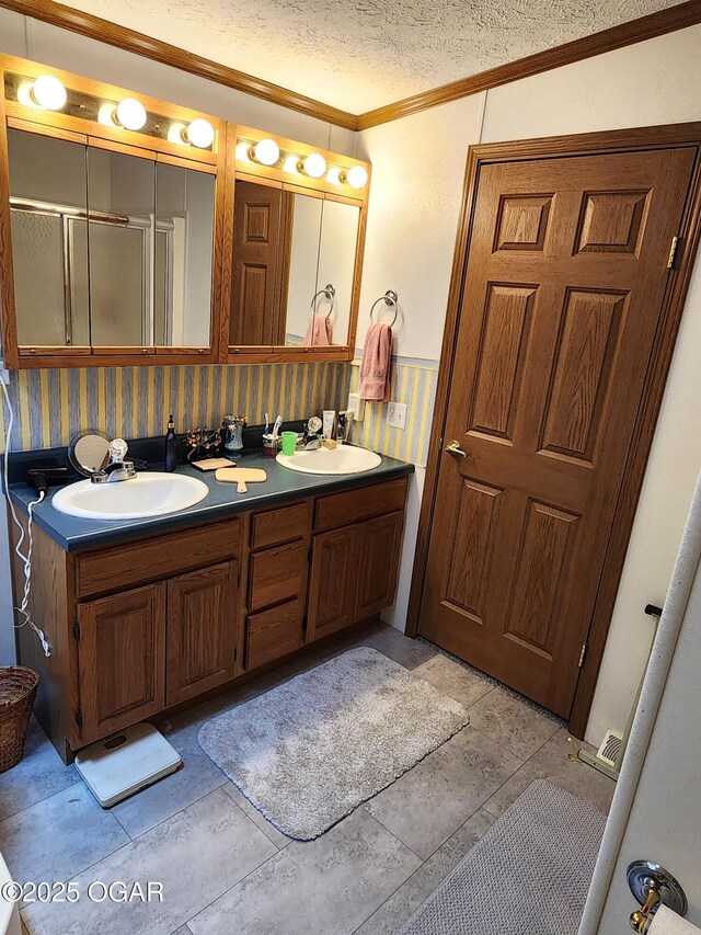 full bathroom with crown molding, double vanity, a textured ceiling, a wainscoted wall, and a shower with shower door
