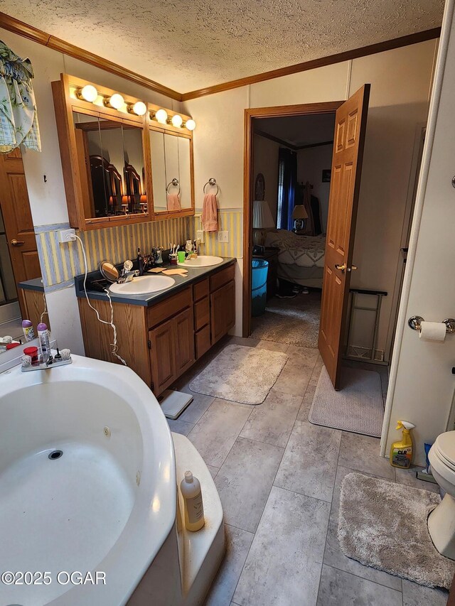 ensuite bathroom with crown molding, wainscoting, double vanity, a textured ceiling, and a whirlpool tub
