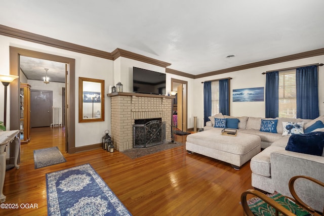 living room featuring radiator, wood finished floors, a brick fireplace, crown molding, and baseboards