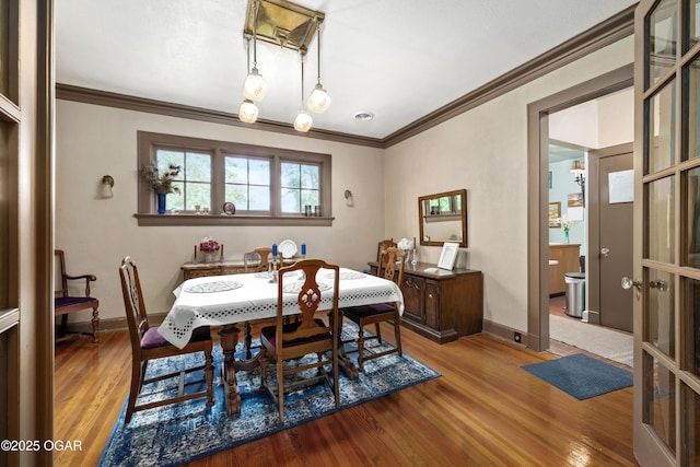 dining area featuring wood finished floors, ornamental molding, and baseboards