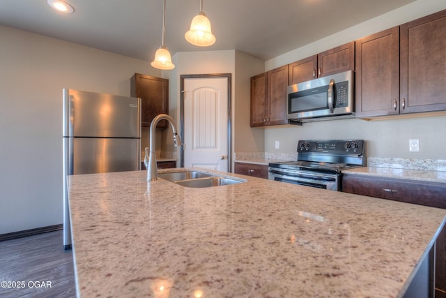 kitchen featuring appliances with stainless steel finishes, a sink, dark wood-type flooring, pendant lighting, and light stone countertops