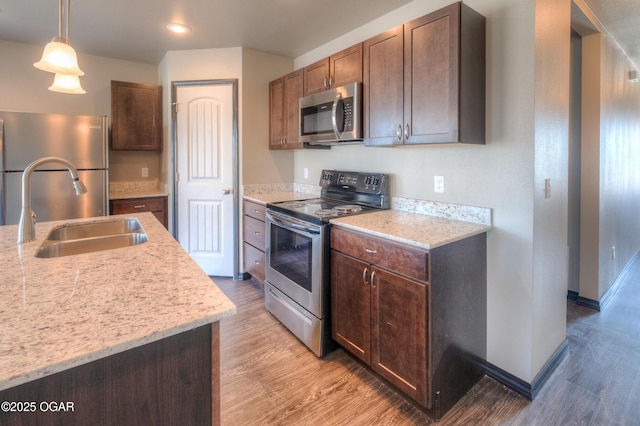 kitchen with stainless steel appliances, a sink, light wood-style flooring, pendant lighting, and recessed lighting