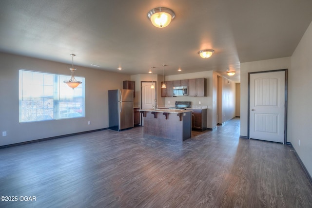 kitchen with stainless steel appliances, a breakfast bar area, a kitchen island, and dark wood-style flooring