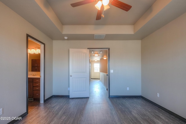 unfurnished bedroom featuring dark wood-type flooring, a tray ceiling, and baseboards