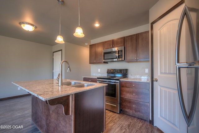 kitchen featuring appliances with stainless steel finishes, a sink, dark wood-style flooring, a kitchen island with sink, and light stone countertops
