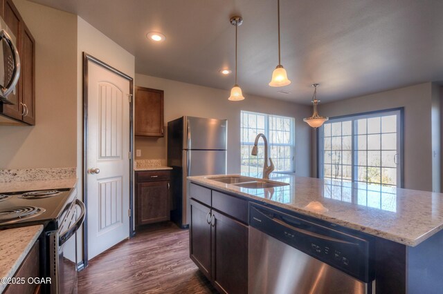 kitchen featuring appliances with stainless steel finishes, a sink, dark wood-type flooring, light stone countertops, and pendant lighting