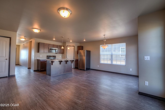 kitchen with appliances with stainless steel finishes, a kitchen bar, open floor plan, light countertops, and a kitchen island