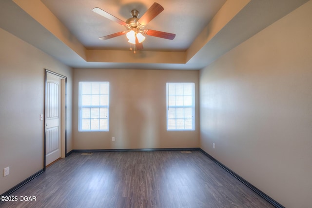unfurnished room with a ceiling fan, wood finished floors, a tray ceiling, and baseboards