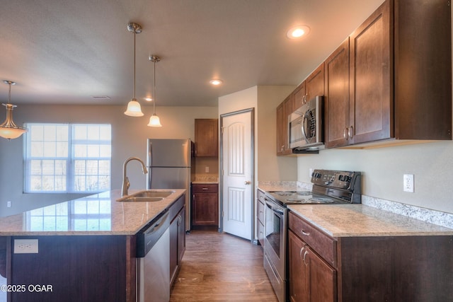 kitchen with stainless steel appliances, a sink, dark wood finished floors, a center island with sink, and decorative light fixtures