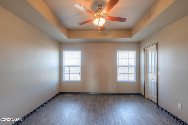 spare room featuring wood finished floors, baseboards, a ceiling fan, and a tray ceiling