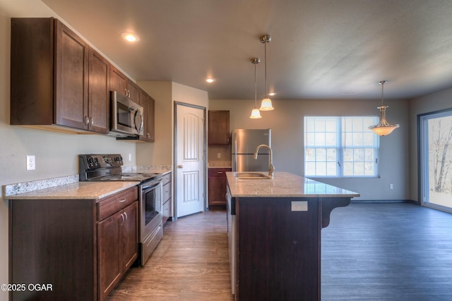 kitchen with stainless steel appliances, wood finished floors, a kitchen bar, a sink, and a center island with sink