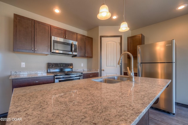 kitchen with stainless steel appliances, a sink, dark wood-style floors, hanging light fixtures, and light stone counters