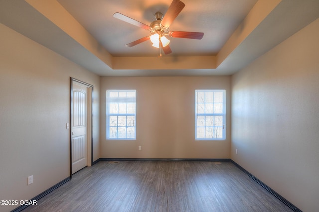 spare room featuring wood finished floors, a raised ceiling, a ceiling fan, and baseboards