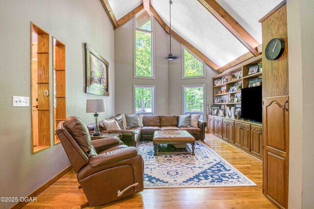 living area with beam ceiling, light wood-style flooring, high vaulted ceiling, baseboards, and a textured wall