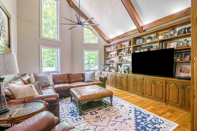living room with ceiling fan, light wood finished floors, a textured ceiling, high vaulted ceiling, and beamed ceiling