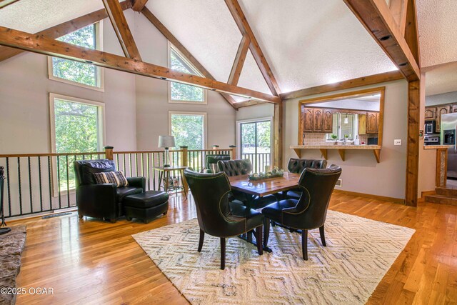 dining area with beam ceiling, high vaulted ceiling, light wood-style flooring, and baseboards