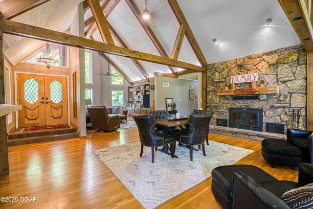 dining space featuring a stone fireplace, high vaulted ceiling, beam ceiling, a chandelier, and wood finished floors