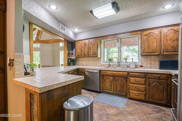 kitchen featuring stainless steel appliances, a sink, tasteful backsplash, a textured ceiling, and a peninsula