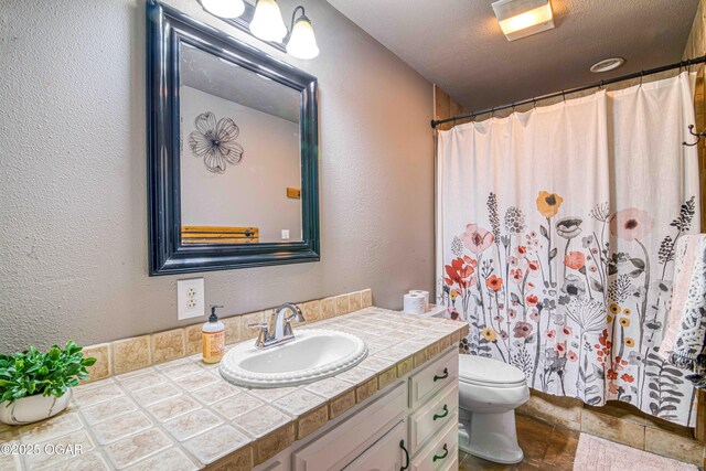 full bathroom with toilet, a textured wall, vanity, and curtained shower