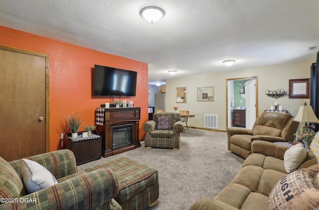 carpeted living room featuring a textured ceiling and a glass covered fireplace