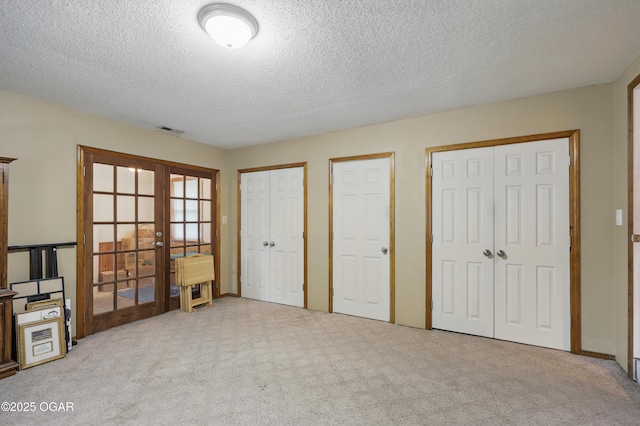 unfurnished bedroom featuring french doors, carpet, multiple closets, and a textured ceiling
