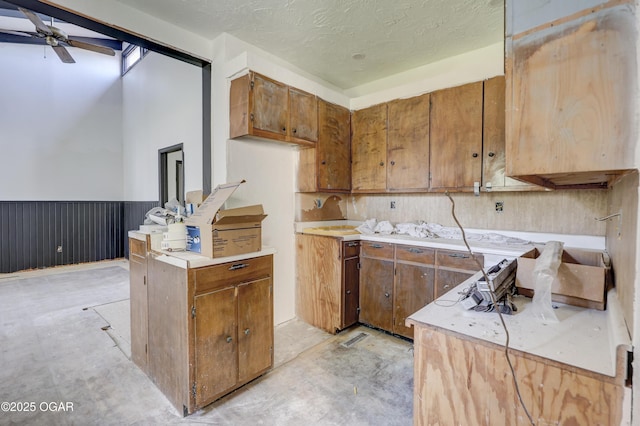 1514 Roosevelt Ave, Joplin, MO 64801 - kitchen with brown cabinetry, light countertops, a wainscoted wall, ceiling fan, and a textured ceiling