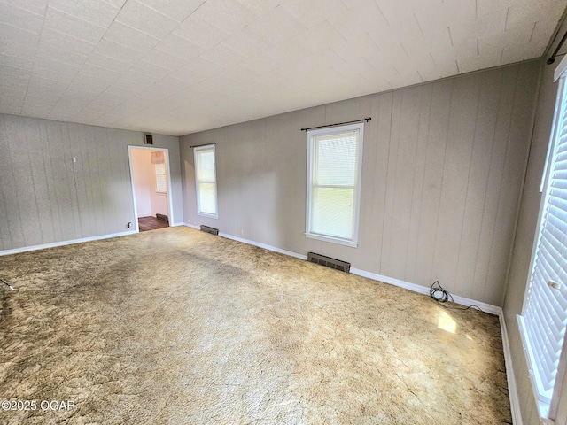 carpeted spare room with baseboards and wood walls
