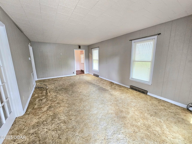 unfurnished living room featuring carpet floors, wooden walls, and baseboards