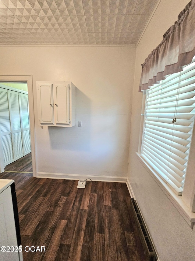 unfurnished dining area featuring ornamental molding, dark wood finished floors, and baseboards