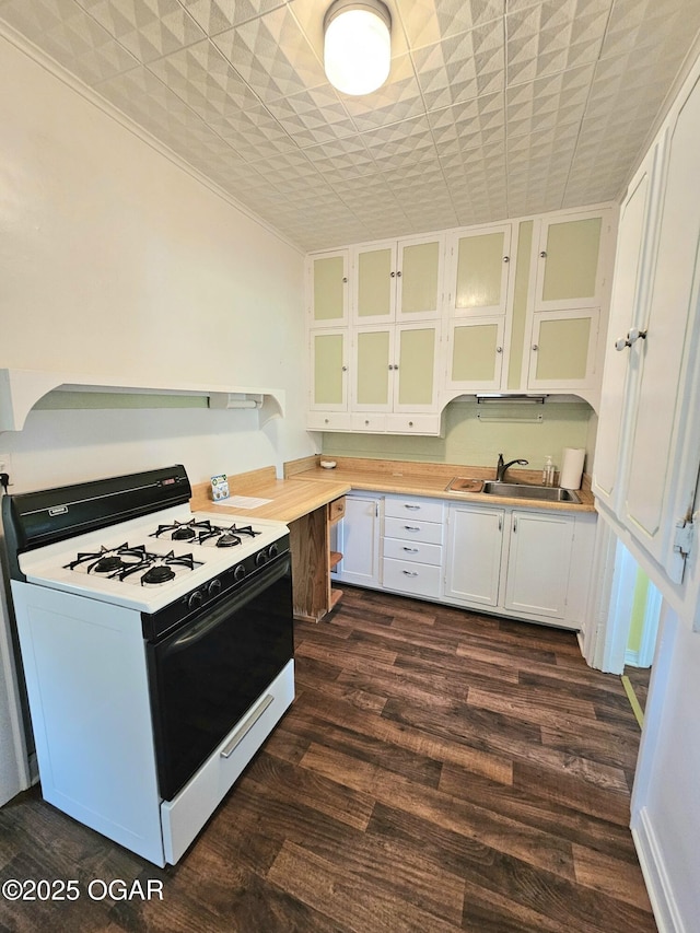 kitchen with white gas range oven, light countertops, a sink, white cabinets, and dark wood-type flooring