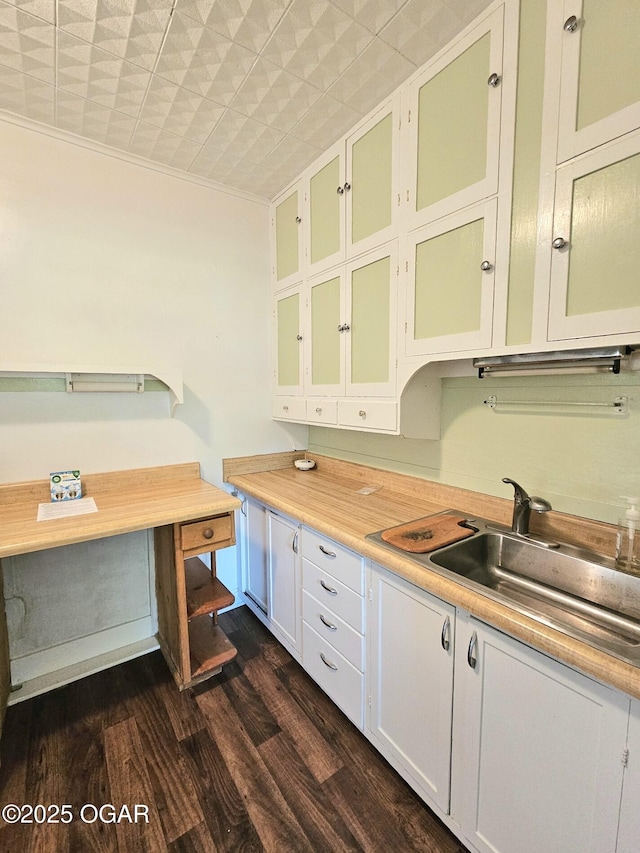 kitchen with light countertops, dark wood finished floors, a sink, glass insert cabinets, and ornamental molding