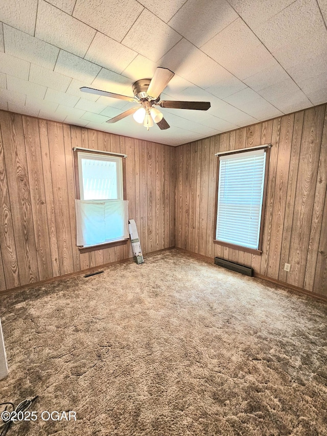 carpeted spare room with ceiling fan and wood walls