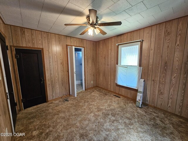 unfurnished bedroom featuring carpet floors, wooden walls, baseboards, and a ceiling fan
